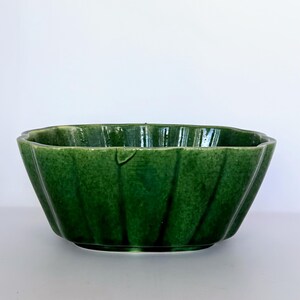 May include: A green ceramic bowl with a fluted design. The bowl has a glossy finish and a wide, open shape. The color is a deep, rich green, and the bowl appears to be in good condition. The bowl is likely for decorative or serving purposes.