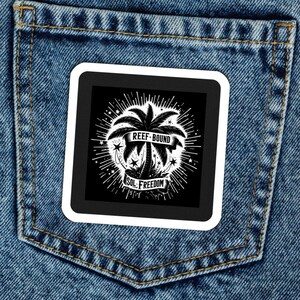 May include: A white patch with black text and a palm tree graphic is sewn onto the back pocket of a pair of blue denim jeans. The text reads "Reef-Bound" and "Sol Freedom".