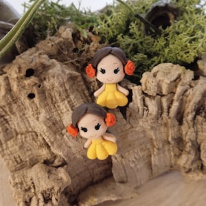 Può includere: Un paio di orecchini in pasta polimerica con una bambina con i capelli castani, un vestito giallo e fiori arancioni.