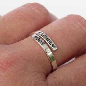 May include: A silver ring with the names "Rachel" and "Joy" engraved on it, separated by a heart symbol.