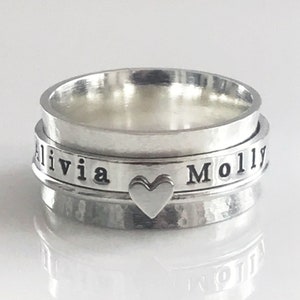 May include: A silver spinning ring with the names Olivia and Molly engraved on it. A small heart charm is attached to the ring.