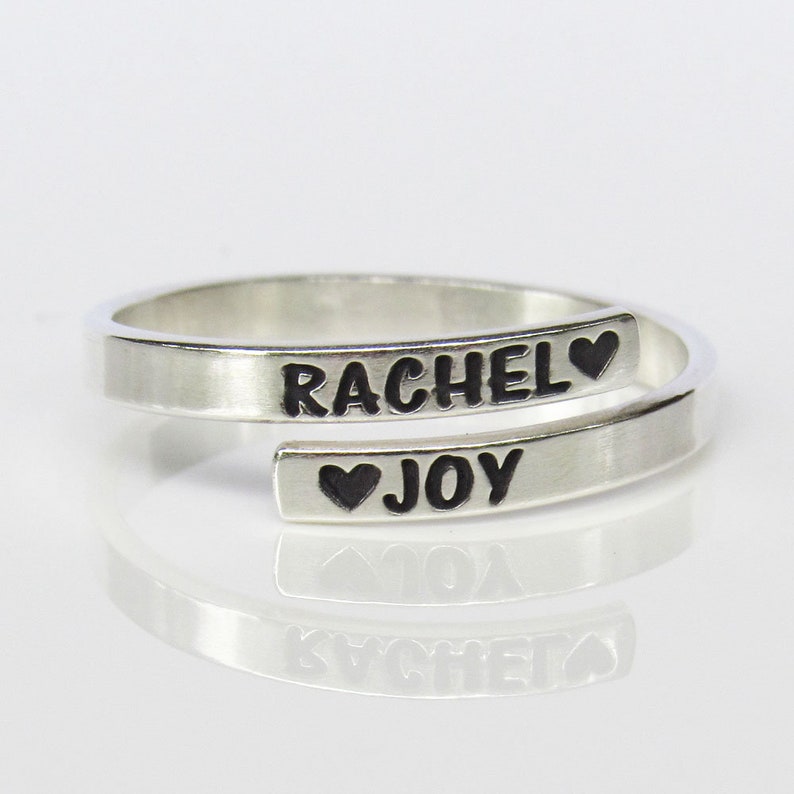 Ring pictured here is the Sterling silver adjustable ring on a white backdrop. The top of the ring reads RACHEL black heart symbol and the bottom reads black heart symbol JOY.