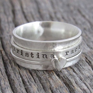 May include: A silver spinning ring engraved with the names "Christina" and "Rachel". The ring features a small heart charm.