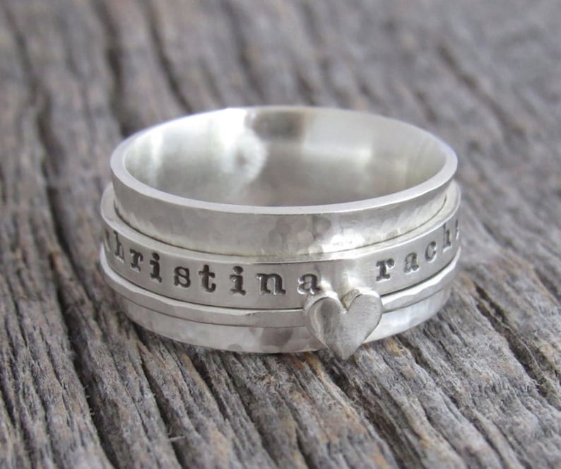 May include: A silver spinning ring engraved with the names "Christina" and "Rachel". The ring features a small heart charm.