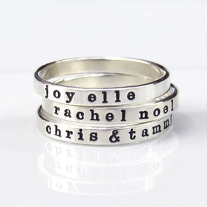 May include: Four silver stacking rings with the names "joy elle", "rachel noel", "chris & tamm" engraved on them.