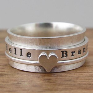 May include: A silver spinning ring engraved with the names "Belle" and "Brand". The ring features a heart-shaped design in the centre.