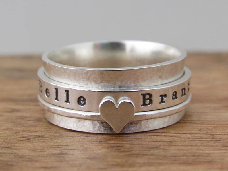 May include: A silver spinning ring engraved with the names "Belle" and "Brand". The ring features a heart-shaped design in the centre.