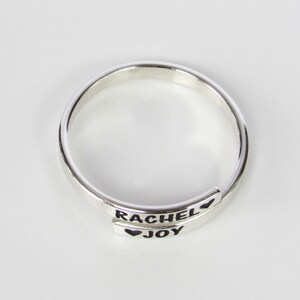 May include: A silver ring with the names "Rachel" and "Joy" engraved on it, separated by a heart symbol.