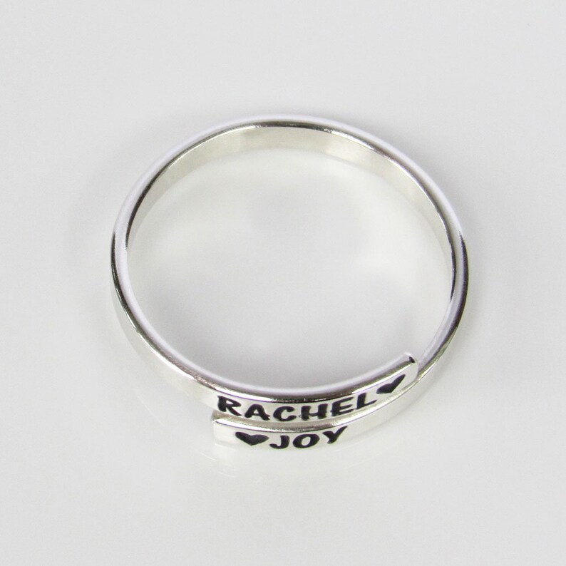 May include: A silver ring with the names "Rachel" and "Joy" engraved on it, separated by a heart symbol.