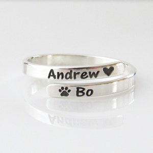 May include: Silver ring with the names "Andrew" and "Bo" engraved on it. The ring also has a heart and a paw print engraved on it.