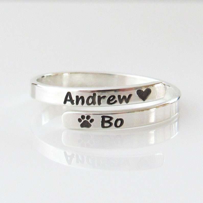May include: Silver ring with the names "Andrew" and "Bo" engraved on it. The ring also has a heart and a paw print engraved on it.