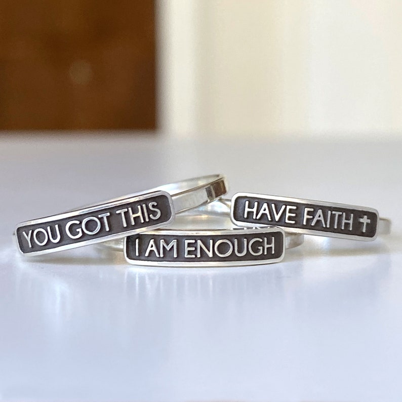 Plate rings pictured here have sayings on them. The ring to the left says YOU GOT THIS. The ring in the middle says I AM ENOUGH. The ring to the right says HAVE FAITH with a cross after.