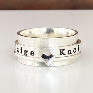 May include: Silver spinning ring engraved with the names "Kaci" and "Paige", separated by a small heart charm.