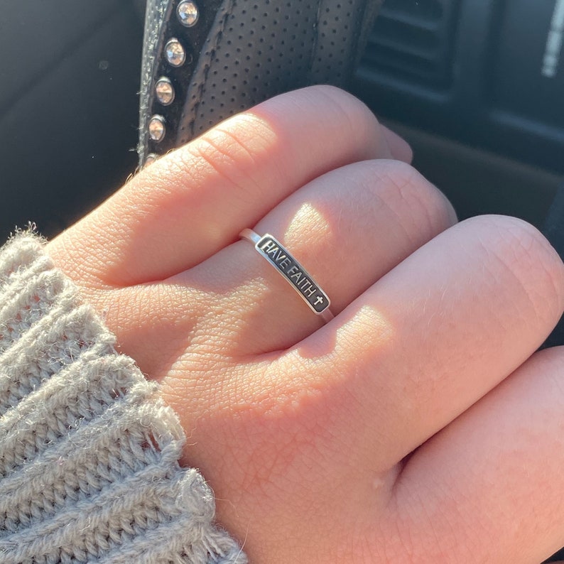 May include: A silver ring with a black rectangular band that says "HAVE FAITH" with a cross symbol.