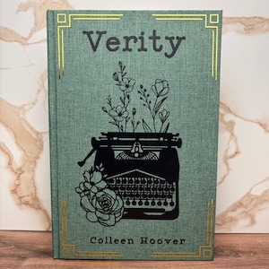May include: A hardcover book titled "Verity" by Colleen Hoover. The book has a teal cover with a gold border and a black illustration of a typewriter with flowers. The title is in a dark gray font.