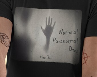 Op de afbeelding: Zwart T-shirt met een afbeelding van een handafdruk en de tekst "National Paranormal Day May 3rd".