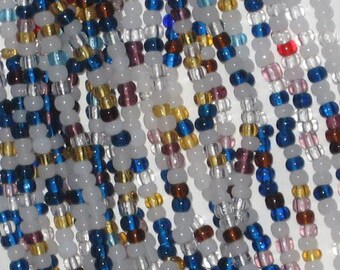 Könnte beinhalten: Nahaufnahme einer mehrfarbigen Perlenkette mit weißen, blauen, goldenen, braunen und rosa Perlen. Die Perlen sind in einem zufälligen Muster angeordnet.