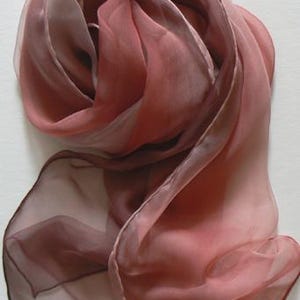 Puede incluir: Una bufanda transparente con un degradado de colores rosa, marrón y blanco. La bufanda está hecha de una tela suave y fluida, perfecta para añadir un toque de elegancia a cualquier atuendo.