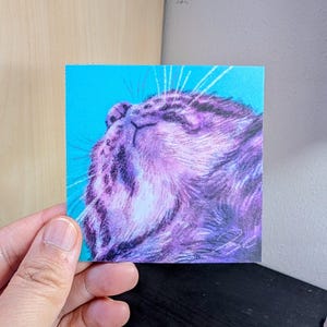 May include: A close-up of a purple cat's face against a bright blue background. The cat's eyes are closed and its mouth is slightly open, as if it is sleeping or dreaming. The cat's fur is soft and fluffy, and its whiskers are long and prominent.