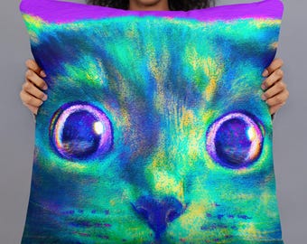 May include: A colorful pillow with a close-up image of a cat's face. The cat's eyes are large and blue with a green, yellow, and purple background.