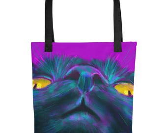 May include: A tote bag with black handles featuring a vibrant, close-up digital painting of a cat face. The cat has glowing yellow eyes and dark fur rendered in shades of blue, purple, and teal against a bright magenta background.