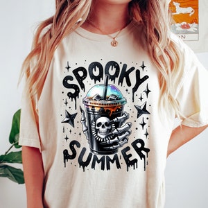 May include: A white t-shirt with a black and white graphic of a skeleton hand holding a cup of iced coffee. The text "Spooky Summer" is written above the cup.