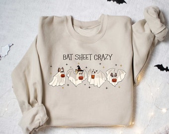 May include: A beige sweatshirt with the text "Bat Sheet Crazy" printed on the front. The text is in black and is surrounded by small gold stars. There are four cartoon bats wearing ghost costumes and holding jack-o'-lanterns.
