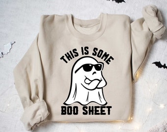 May include: A beige sweatshirt with a black and white graphic of a ghost wearing sunglasses and the text "This is some boo sheet".