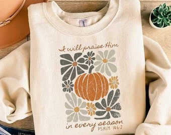 May include: A beige sweatshirt with a graphic design of flowers, a pumpkin, and the text "I will praise Him in every season Psalm 146:2".