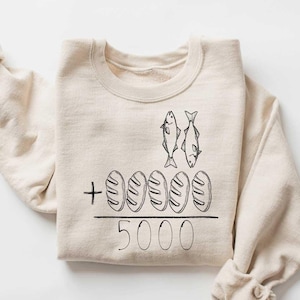 May include: A beige sweatshirt with a black graphic of two fish and five loaves of bread with the text " + 5000" printed on the front.