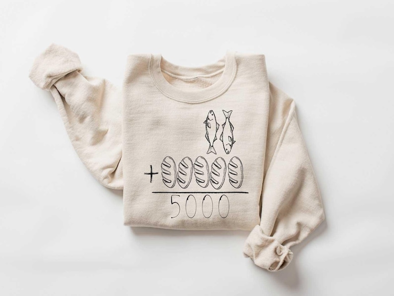 May include: A beige sweatshirt with a black graphic of two fish and five loaves of bread with the text " + 5000" printed on the front.