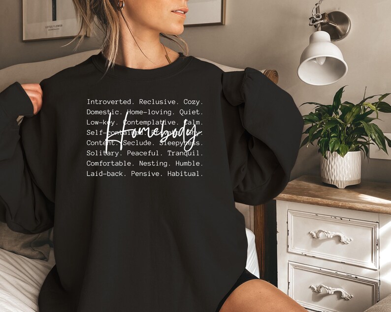 May include: Black sweatshirt with white text that reads "Introverted. Reclusive. Cozy. Domestic. Home-loving. Quiet. Low-key. Contemplative. Calm. Self-Homebody Content. Seclude. Sleepy. Solitary. Peaceful. Tranquil. Comfortable. Nesting. Humble. Laid-back. Pensive. Habitual."