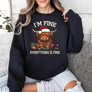 May include: Black sweatshirt with a graphic of a Highland cow wearing a Santa hat and surrounded by Christmas lights. The text "I'm Fine Everything is Fine" is printed below the image.