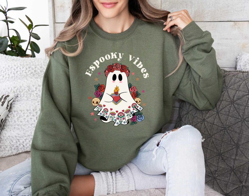 May include: A green sweatshirt with a white ghost wearing a floral crown and holding a heart. The text "Spooky Vibes" is printed on the sweatshirt.