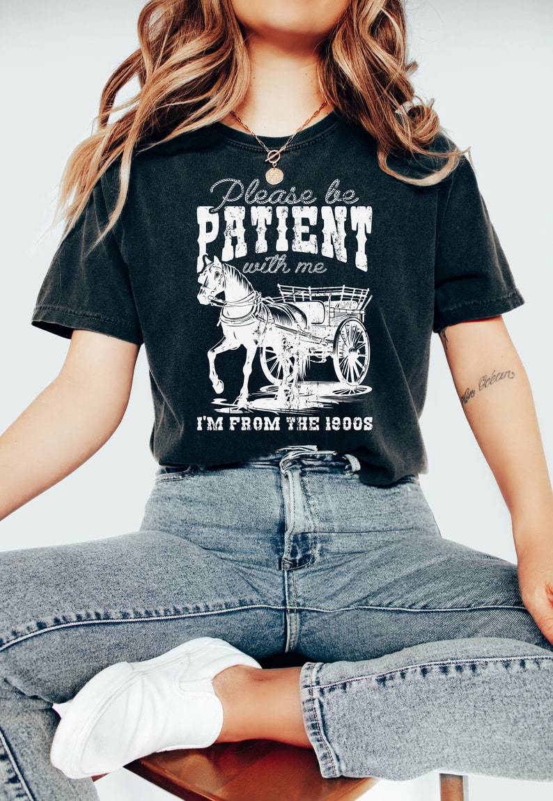 K&ouml;nnte beinhalten: Ein schwarzes T-Shirt mit einer wei&szlig;en Grafik einer Pferdekutsche und dem Text "Please be PATIENT with me I'M FROM THE 1900s".
