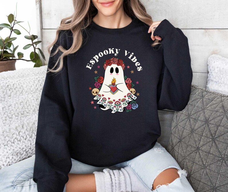 May include: Black sweatshirt with a white ghost wearing a floral crown and holding a heart. The text "Spooky Vibes" is printed in white above the ghost.