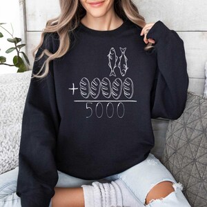 May include: Black sweatshirt with a white graphic of two fish and five loaves of bread with the text " + 5000".