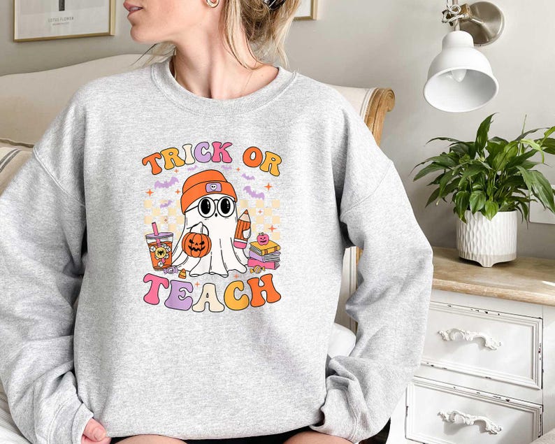 May include: Gray sweatshirt with a ghost wearing a hat and holding a book. The text "Trick or Teach" is printed on the front of the sweatshirt.