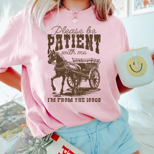 K&ouml;nnte beinhalten: Rosa T-Shirt mit einem braunen Pferdewagen-Motiv und dem Text "Please be PATIENT with me I'M FROM THE 1900s".