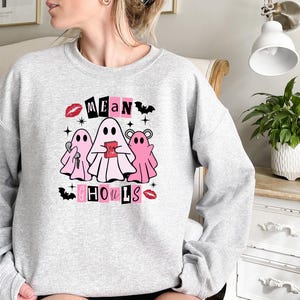 May include: A gray sweatshirt with a pink and black graphic design featuring ghosts and the text "Mean Ghouls".