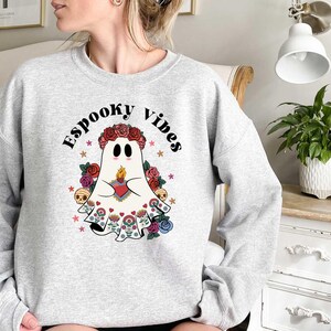 May include: A gray sweatshirt with a white ghost wearing a floral crown and holding a heart. The text "Spooky Vibes" is printed on the sweatshirt.