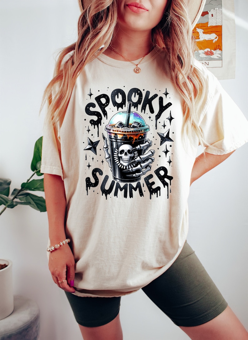 May include: A white t-shirt with a black and white graphic of a skeleton hand holding a cup of iced coffee. The text "Spooky Summer" is written above the cup.