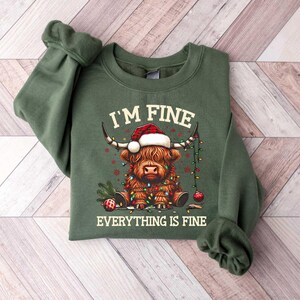 May include: Green sweatshirt with a festive Highland cow wearing a Santa hat and Christmas lights. The text "I'm Fine Everything is Fine" is printed on the sweatshirt.