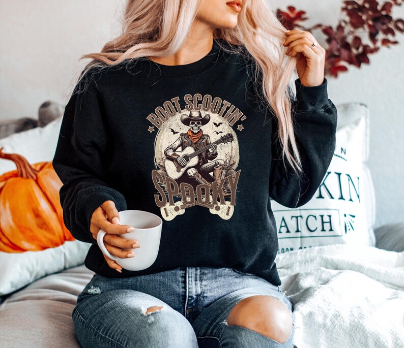 May include: A black sweatshirt with a graphic of a skeleton playing a guitar. The text on the graphic says "Boot Scootin' Spooky".