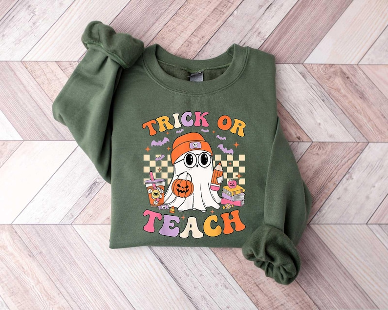 May include: Green sweatshirt with a ghost wearing a hat and holding a pumpkin. The text "Trick or Teach" is printed on the front.