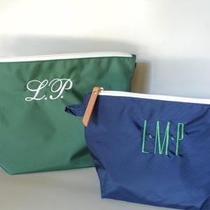 May include: A dark green pouch with white embroidered initials L.P. and a navy blue pouch with green embroidered initials L.M.P. Both pouches feature a white zipper closure and a tan leather-like pull tab attached to the navy blue zipper.