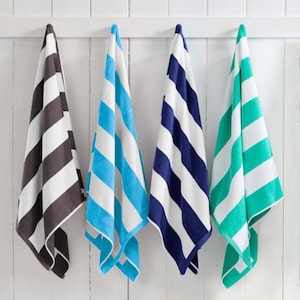 May include: Four beach towels hanging on a white wall. The towels are striped in various colors: brown and white, light blue and white, navy blue and white, and teal and white. The towels are folded over a wooden bar.