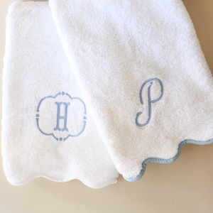 May include: Two white terry cloth towels with scalloped edges trimmed in light blue. One towel features an embroidered light blue letter H inside a decorative frame, while the other towel displays an embroidered light blue cursive letter P.