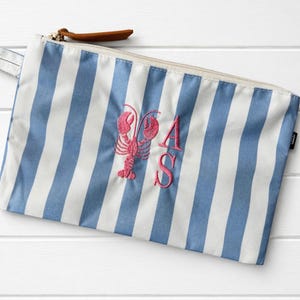 May include: A rectangular zippered pouch featuring a blue and white vertical striped pattern. The center of the pouch is embroidered with a pink lobster graphic and the letters A and S in a matching pink thread. A brown leather zipper pull is attached.