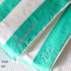 May include: Teal and white striped beach towels with embroidered names in pink script. One towel reads "Lauren" and the other reads "Lita". The towels are folded and stacked, showcasing the soft texture and color scheme.